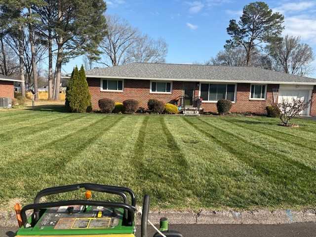 Early-spring lawn mowed in bold straight stripes in front of a brick ranch home