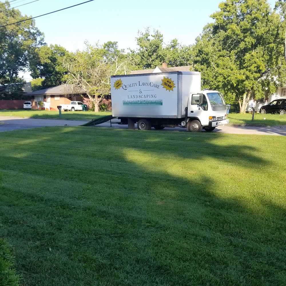 Company box truck parked on a residential street behind a bright green, freshly cut lawn