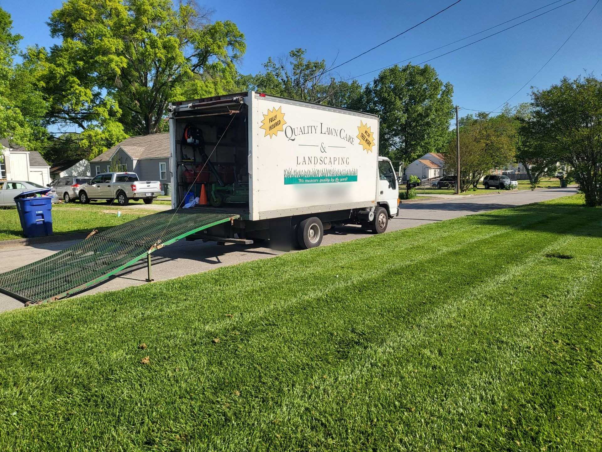 Quality Lawn Care & Landscaping box truck with its loading ramp down beside a freshly striped lawn