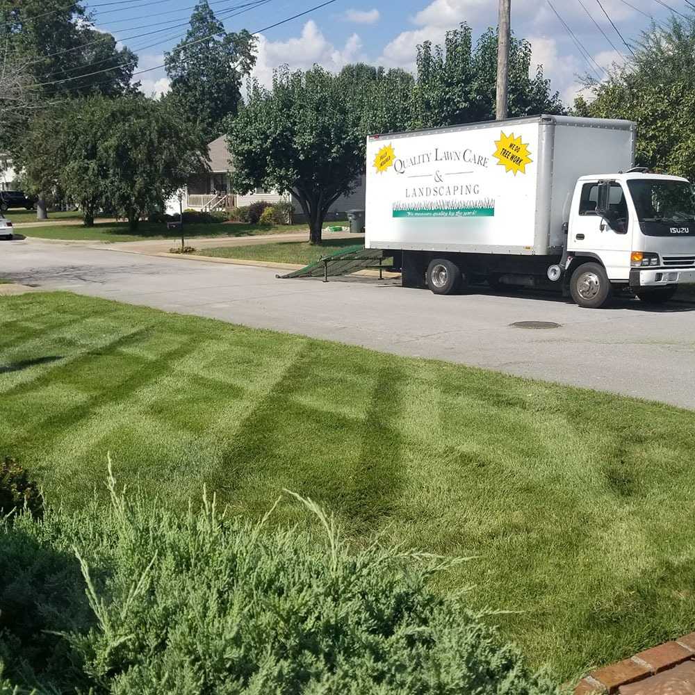 Striped lawn and trimmed shrubs in the foreground with the company box truck parked on the street